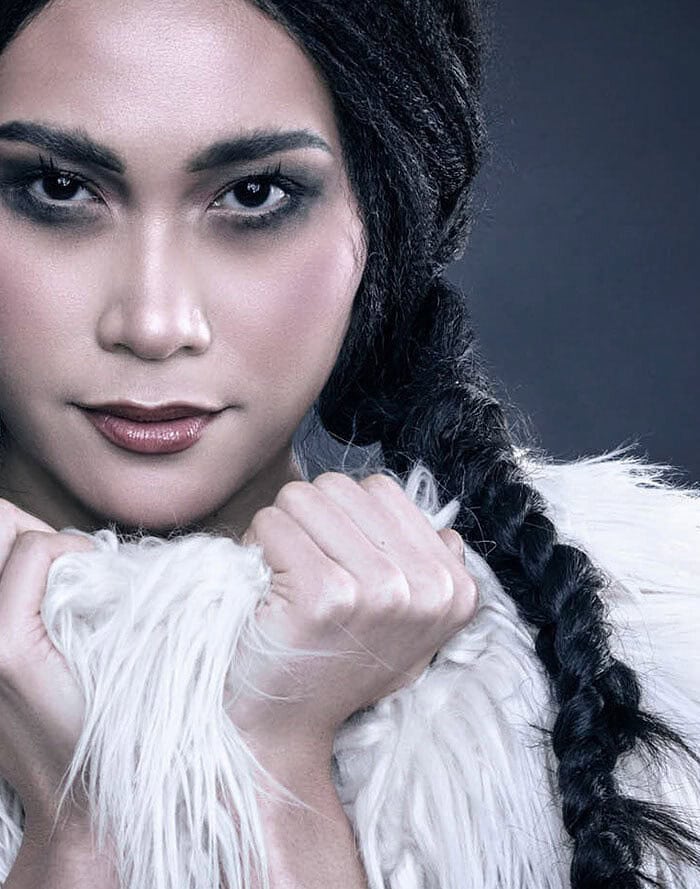 Close-up beauty portrait of a model with black braids holding a white shaggy fur garment beneath her face.