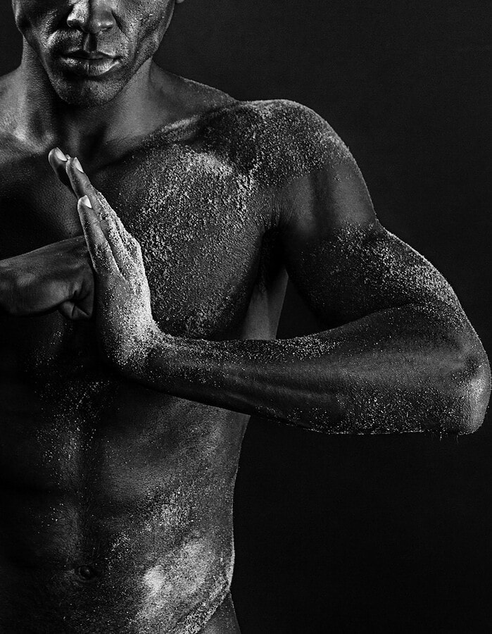 Study Cropped black-and-white portrait of a male model pressing his hands together across a sand-textured torso.