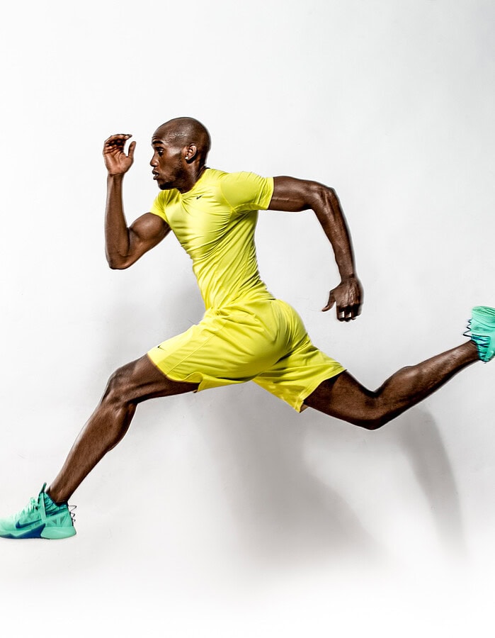 Athletic male model airborne in a running pose wearing yellow sportswear and mint-green sneakers.