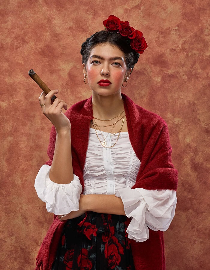 Woman with red roses in her hair wearing a red shawl and white ruffled blouse while holding a cigar.